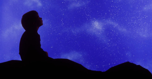 Square image of a small child in profile looking up at a star filled night sky.