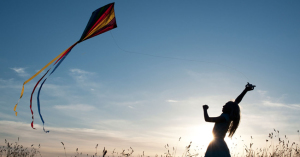 Young Girl having fun flying a multicoloured kite in the English countryside. Silhouette