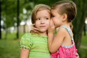 Two twin little sister girls whisper in ear